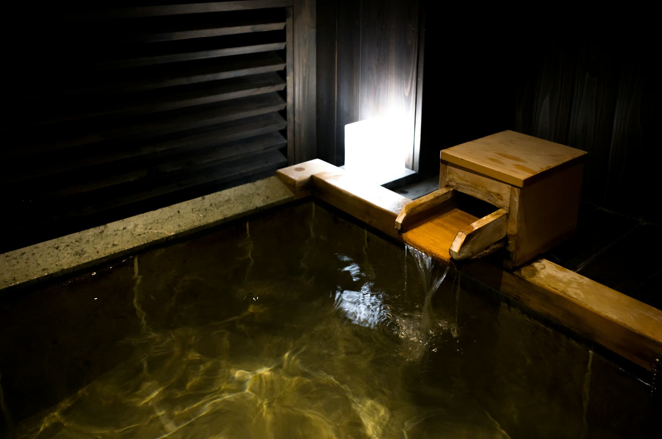 A quiet Japanese onsen bath lit warmly against dark wood